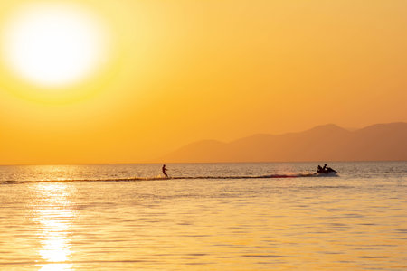 Water skiing, wake, jet ski and golden sun over the sea. Beautiful sunset over the sea. Water skiing athlete. Sportsmen on a jet ski at sea. Golden sky and fantastic sunsetの写真素材