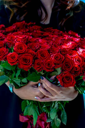 Red roses in the hands of a cute lady. Red thorn roses and woman's hands. A gift for a beloved womanの写真素材