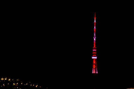 Glowing TV tower in the silence of the night. High multi-colored tower and houses of the night city. Beautiful tower in the night cityの写真素材