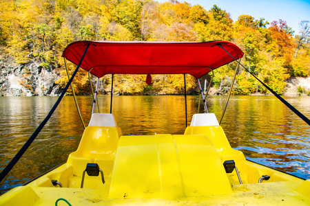 Autumn day, boat in the lake in the autumn forest. Yellow leaves of trees are reflected in the...