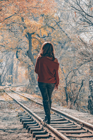 Golden autumn forest and a girl. A girl walks on a train rail in the forest