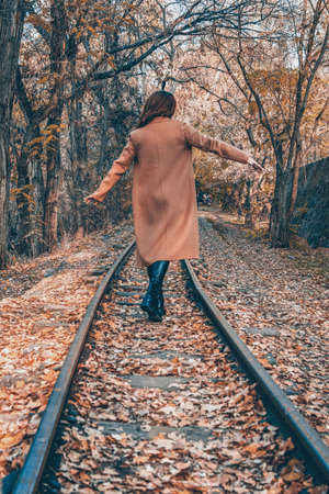 Golden autumn forest and a girl. A girl walks on a train rail in the forestの写真素材