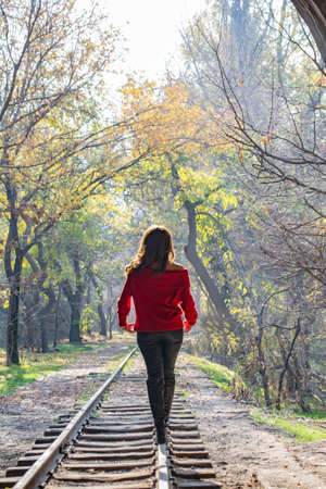 Lonely woman, railways and fairy forest. Beautiful woman walks on the railroad in the autumn forestの写真素材