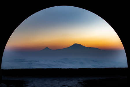 Mountain and arch. The mountain and sunset are visible through the arch. The sun is setting over the mountainの写真素材