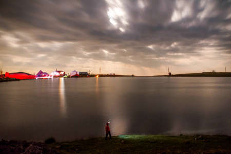 Night sky shining and lake. Night cloudy sky and houses next to the lake. Reflection of the moon on the lake. scenic viewの写真素材