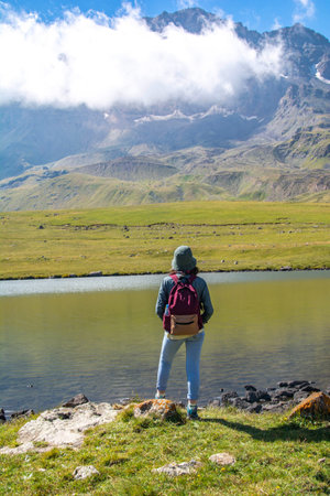 Young woman standing on the edge of a mountain lake and enjoying the viewの写真素材