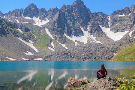 Woman sitting on the edge of a mountain lake and looking at the mountainsの写真素材