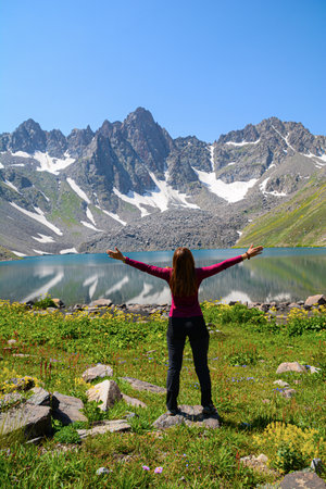 A girl stands on the shore of a mountain lake and looks at the mountainsの写真素材