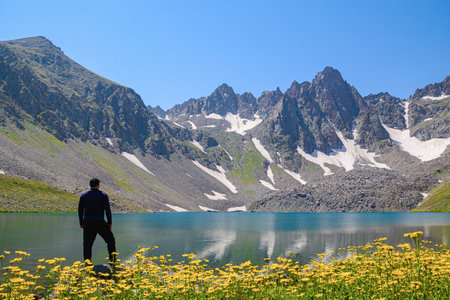 Man standing on the edge of a mountain lake with mountains in the backgroundの写真素材