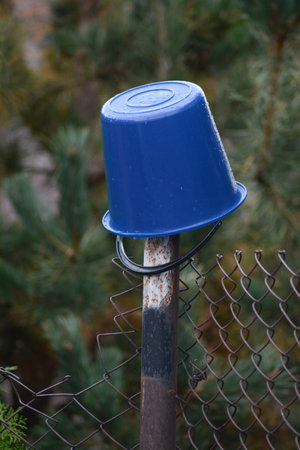 Blue plastic trash can on a chain link fence in the garden.の写真素材