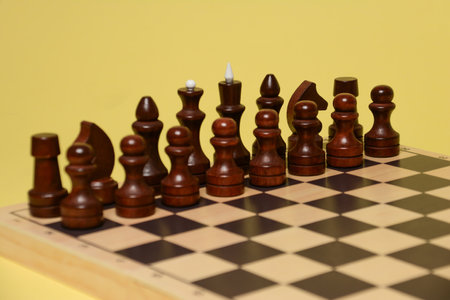 Wooden chess pieces on a chessboard on a yellow background.の写真素材