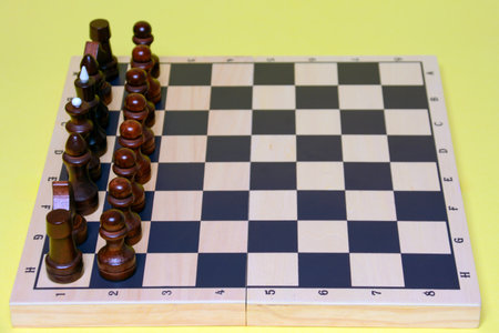 Wooden chess pieces on a chessboard on a yellow background.の写真素材