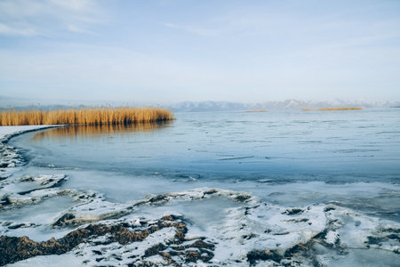 Winter landscape with frozen lake and snow-capped mountains in the backgroundの写真素材