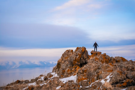 Man standing on top of a rock in the mountains at sunset.の写真素材