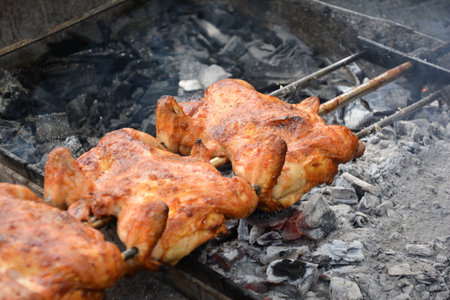 Grilled chicken on a spit over the coals of a barbecueの写真素材