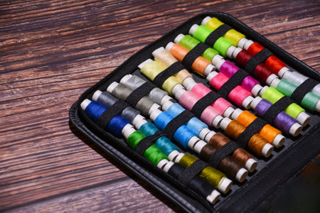 Colorful sewing threads in a black case on a wooden background.