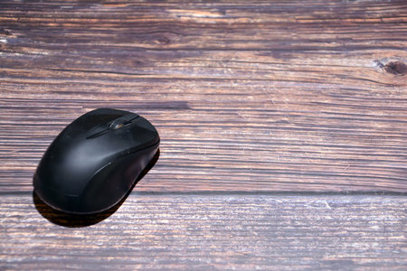 Black computer mouse on wooden background. Top view. Copy space.