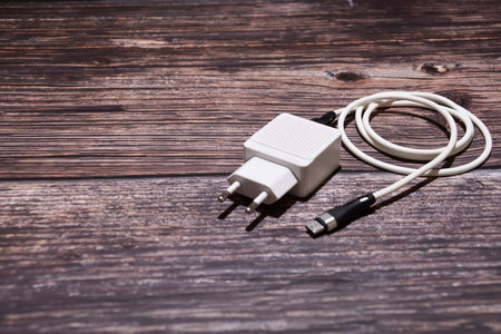 An adapter and USB cable for charging a mobile phone. A white Type-C cable with an adapter on a table. White USB cable on a wooden background.の写真素材