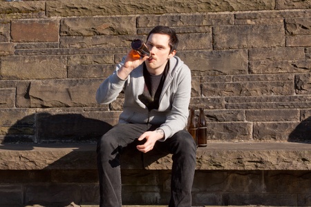 A young man is sitting on a wall drinking beerの写真素材