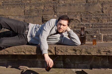 A young guy is lying on a bench drinking beerの写真素材