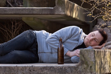 A young man is lying in a park drinking beerの写真素材