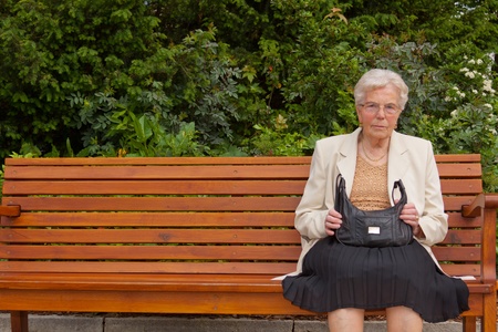 An old lonely woman is sitting on a bench in a parkの写真素材