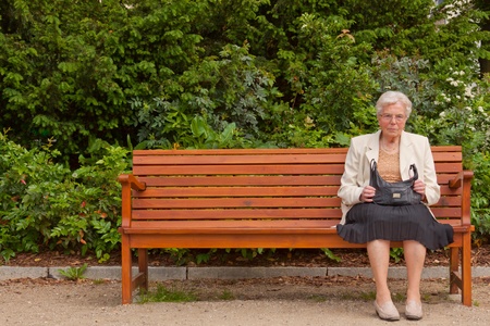 An old lonely woman is sitting on a bench in a parkの写真素材