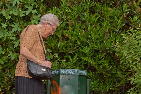 An old lonely woman is looking into garbage canの写真素材