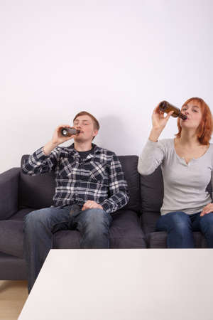 A young couple in love is sitting on the sofa and drinking beerの写真素材