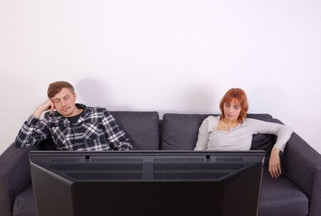 A young couple is sitting on the sofa and watching tellyの写真素材