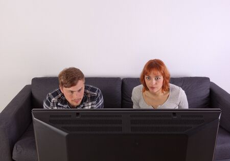 A young couple is sitting on the sofa and watching tellyの写真素材