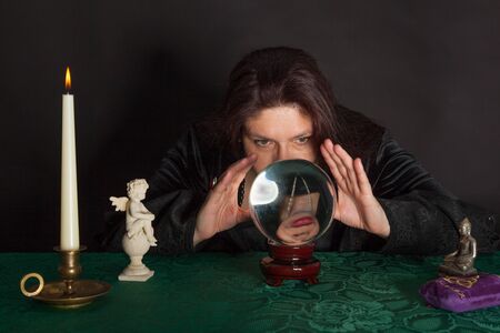 A dark dressed woman is looking into a crystal ballの写真素材