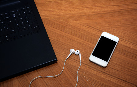 Close up view of white smart phone, earphones and opened laptop.の写真素材