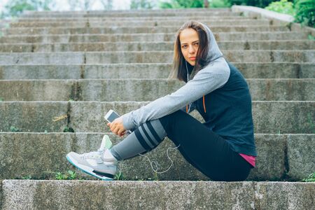 Smiling Athlete with phone relaxing on stairs in the park after workoutの写真素材