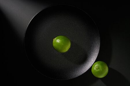 Two limes  in black plate on black background with ray of light            の写真素材