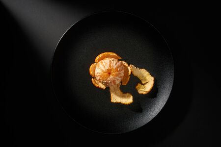 Tangerine in black plate on black background with ray of lightの写真素材