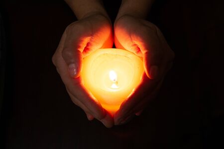 heart formed with hands and a burning candle, yellow image with black backgroundの写真素材