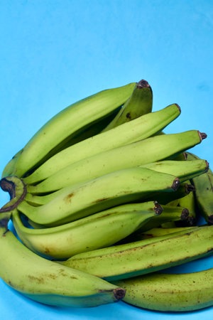 Fresh green banana on blue background, maqueno, barraganete, dominico. hands table knifeの写真素材