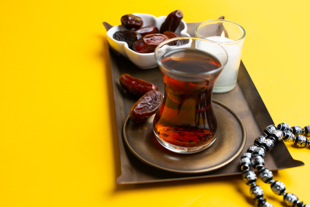 Ramadan Kareem Festival, close up of tasty dates at bowl with rosary and cup of black tea on yellow...
