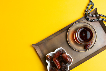 Ramadan Kareem Festival, Dates on wooden bowl with cup of black tea and rosary on yellow backgroundの写真素材