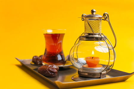Ramadan Kareem Festive, close up of dates on plate with candle lamp and cup of black tea on yellow backgroundの写真素材