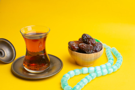 Ramadan Kareem Festival, Dates on wooden bowl with cup of black tea and rosary on yellow backgroundの写真素材