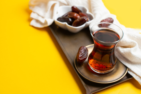 Ramadan Kareem Festival, close up of tasty dates at bowl with rosary and cup of black tea on yellow background.の写真素材