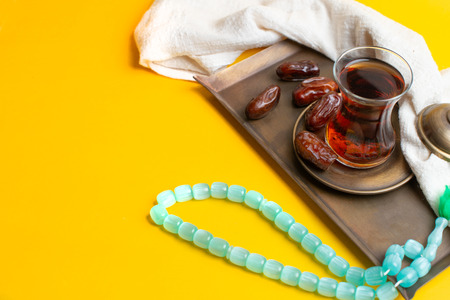 Ramadan Kareem Festival, Dates on wooden bowl with cup of black tea and rosary on yellow backgroundの写真素材