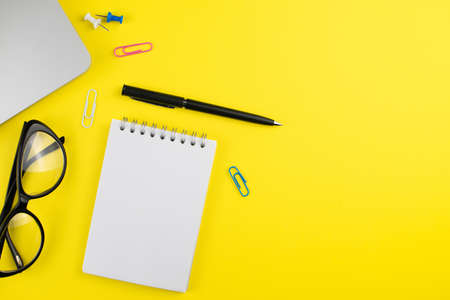 Laptop, black pen, planner notepad, black eye glasses and colorful clips on yellow background. Flat...