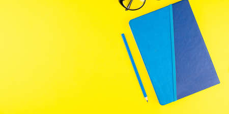 Blue pencil and notepad planner, black eye glasses on yellow background. Flat lay. Copy space....