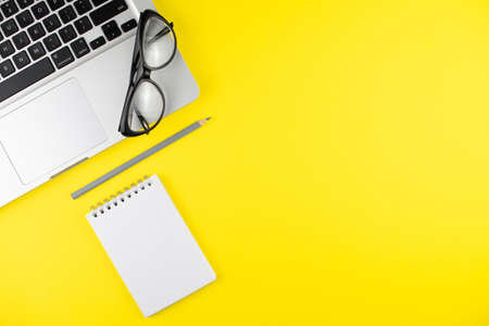Black eye glasses, pencil, laptop, notepad planner on yellow background. Flat lay. Copy space. Workplace in the office.の写真素材