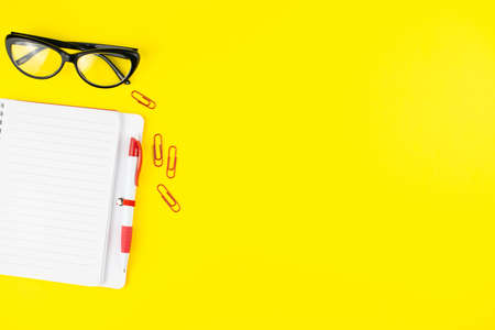Black eye glasses, pen, notepad planner and colorful clips on yellow background. Flat lay. Copy space. Workplace in the office.の写真素材