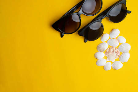 Summer accessories, shells and couple sun glasses on yellow background. Summer, honey moon and sea concept.の写真素材