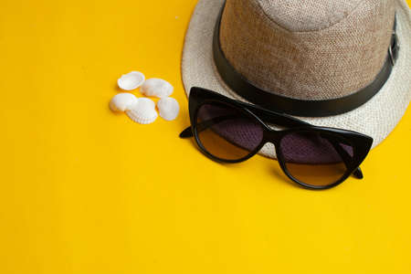 Summer accessories, sea exotic shells, hat and sun glasses on yellow background. Summer vacation and sea concept. Copyspace for textの写真素材